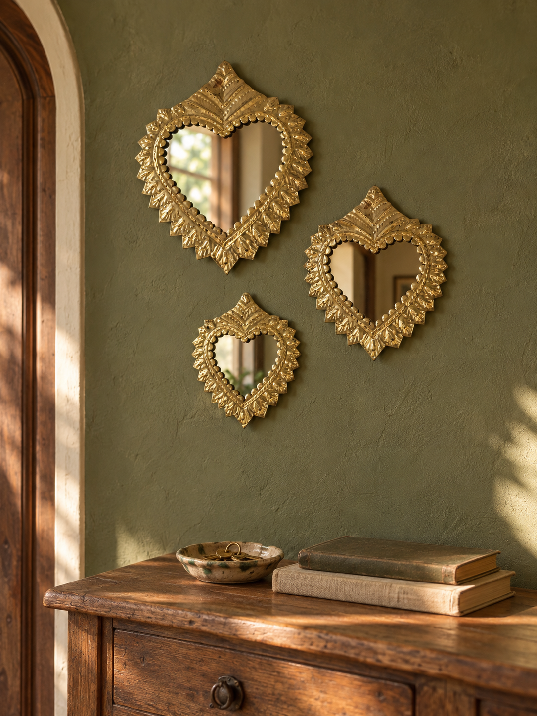 Trois miroirs ex-voto cœur en cuivre présentés dans une entrée bohème sur un mur vert olive