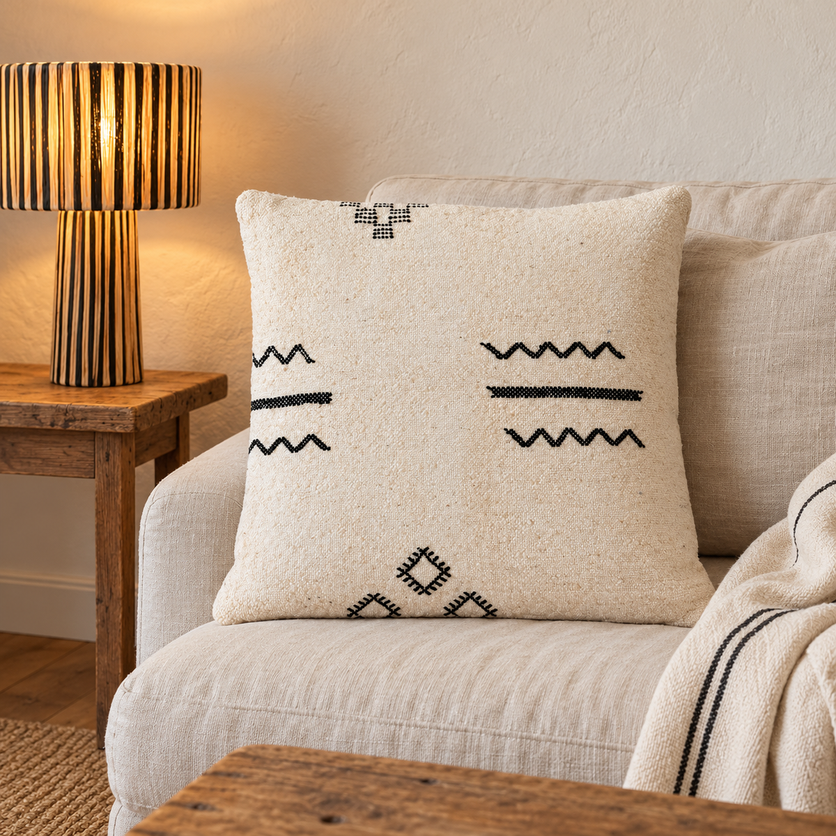 Coussin kilim à zigzags noirs sur un canapé écru près d’une lampe en raphia rayé