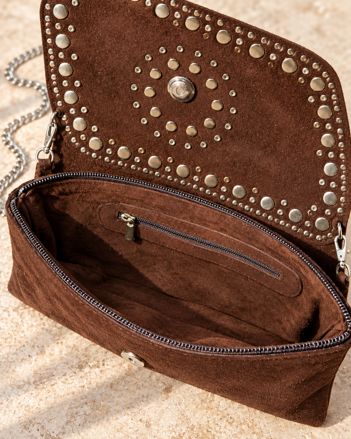 Intérieur de la pochette en daim marron chocolat avec poche zippée, rabat ouvert et attaches de bandoulière argentées