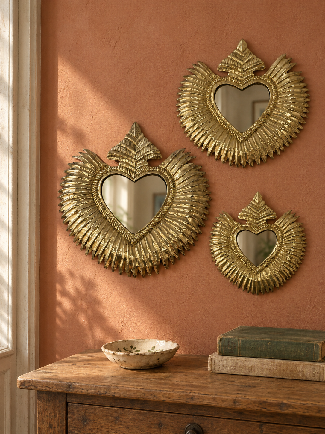 Trois ex-voto cœur sacré rayonnants en cuivre sur un mur terracotta